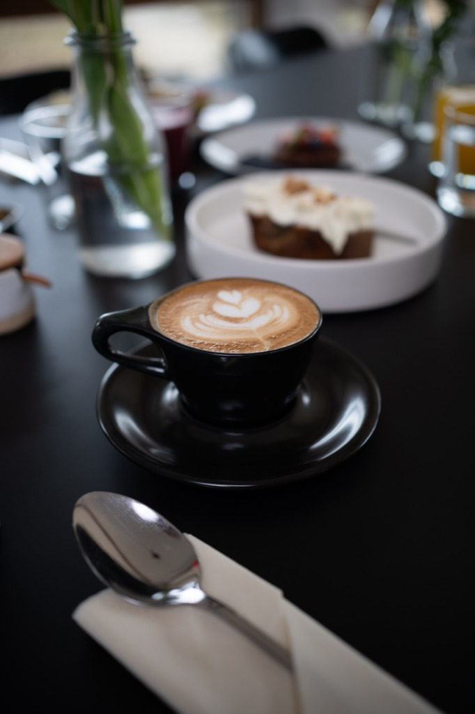 Köstlicher, frisch zubereiteter Cappuccino mit feiner Latte Art in einer schwarzen Tasse auf gedecktem Tisch